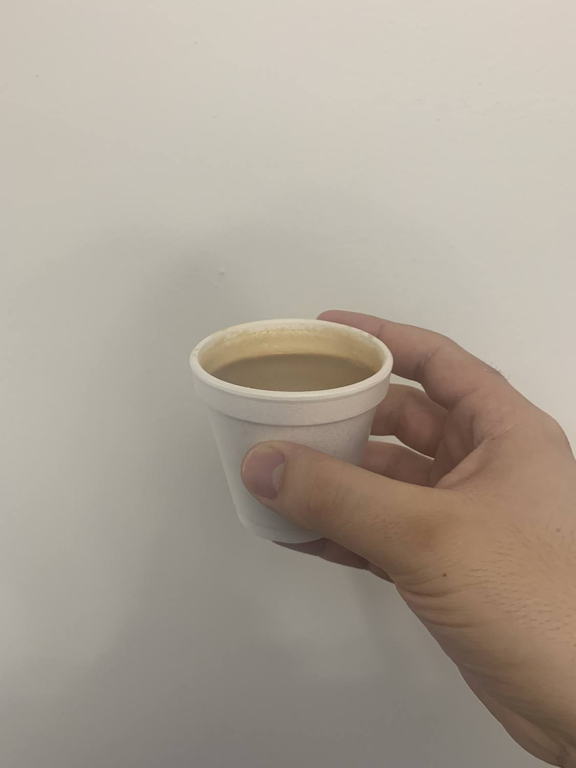 A hand holding a little foam cup of Cuban coffee