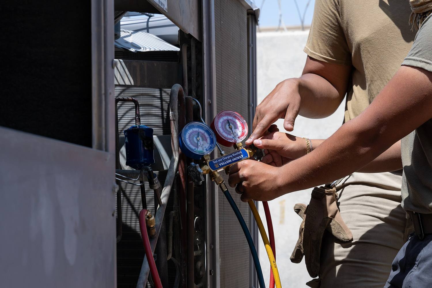 A technician's hands holding refrigerant pressure gauges