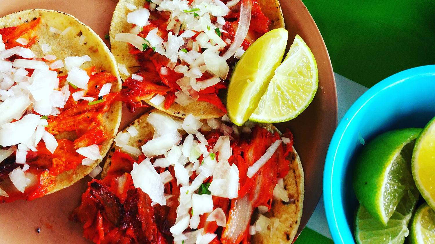 Tacos al pastor topped with onion, with lime wedges on the side