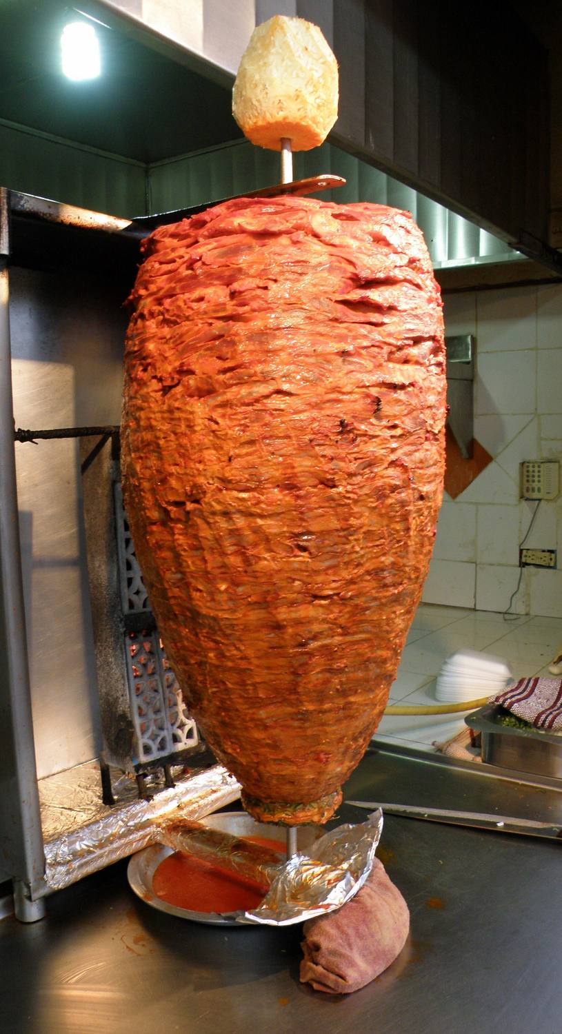 A trompo of al pastor pork on a vertical spit with a pineapple on top