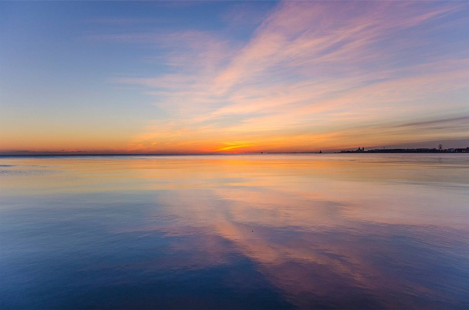 Still water at dawn with soft pink and blue clouds reflected on it