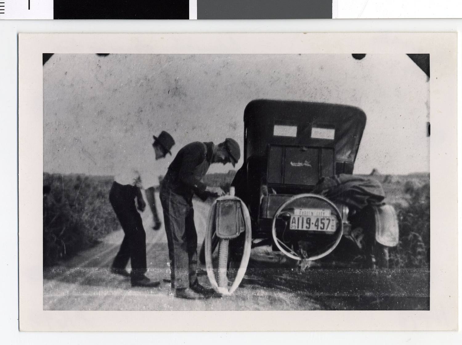 An old black-and-white photo of people changing a tire by the side of the road